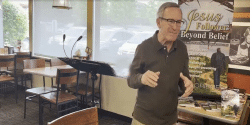 Man speaking in a cafe, with a 'Jesus Followers Beyond Belief' poster in the background.